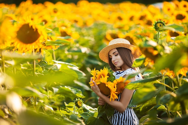 Bella donna bionda nel campo di fiori al tramonto in cappello di paglia