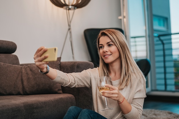 Bella donna bionda seduta sul pavimento e prendendo selfie.