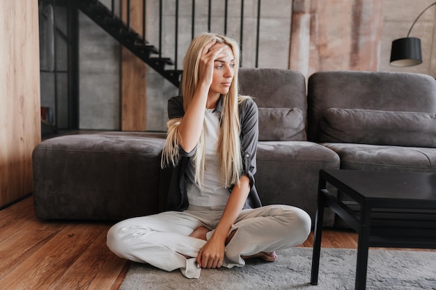 Bella donna bionda stanca seduta sul pavimento a casa che tocca la fronte Casalinga svedese esausta