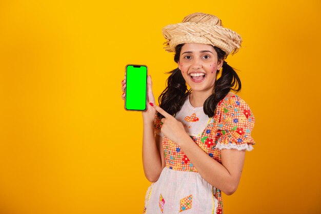 Bella donna brasiliana con abiti da festa junina che tiene smartphone con schermo verde