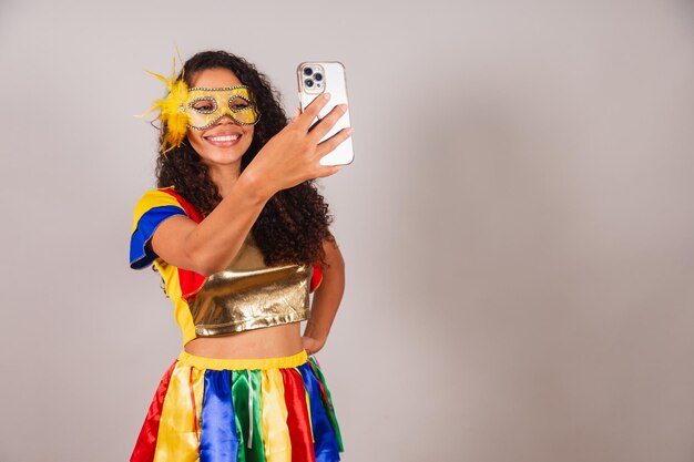 Bella donna brasiliana nera che indossa abiti di carnevale prendendo selfie con lo smartphone