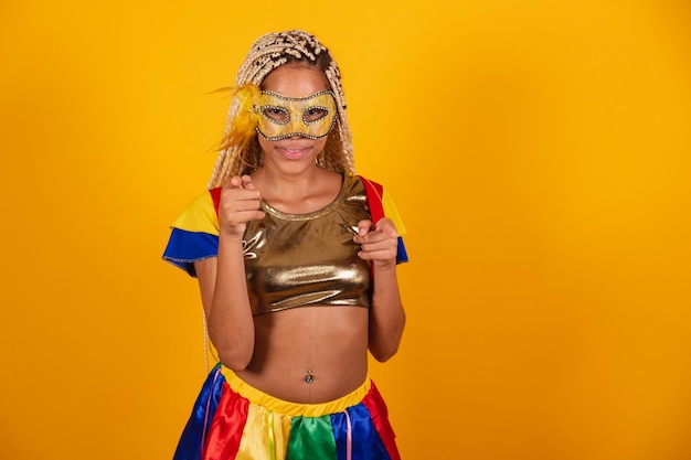 Bella donna brasiliana nera vestita con abiti di carnevale maschera sfondo giallo dito alzato puntato verso la macchina fotografica