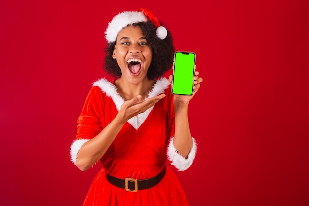 Bella donna brasiliana nera vestita da babbo natale mama claus che mostra lo schermo dello smartphone