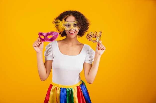 Bella donna brasiliana vestita con abiti di carnevale gonna colorata e camicia bianca con in mano due maschere che invitano alla festa