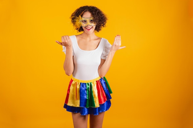 Bella donna brasiliana vestita di carnevale abiti gonna colorata e camicia bianca che indossa mascara invitante con le mani