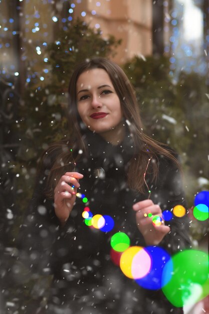 Bella donna bruna che cammina per strada vicino alle ghirlande colorate con fiocchi di neve