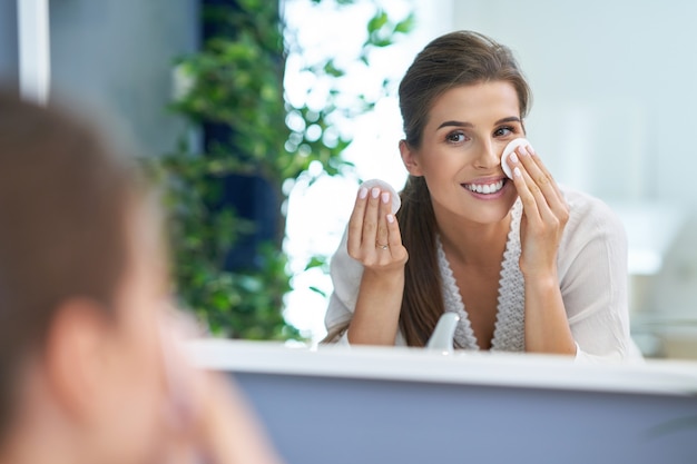 Bella donna bruna che pulisce il viso in bagno