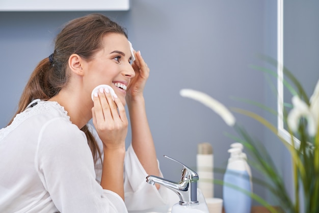 Bella donna bruna che pulisce il viso in bagno