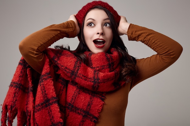 Bella donna bruna in maglione e cappello rosso con grande sciarpa lavorata a maglia