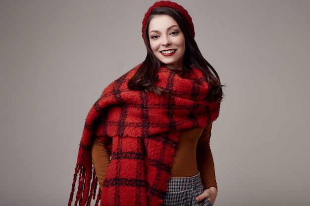 Bella donna bruna in maglione e cappello rosso con grande sciarpa lavorata a maglia