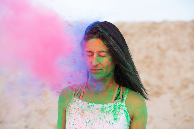 Bella donna bruna in posa con l'esplosione di polvere rosa secca Holi al deserto