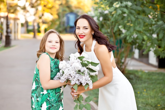 Bella donna bruna mamma con sua figlia che cammina nel parco o nel giardino primaverile tra i lillà in fiore