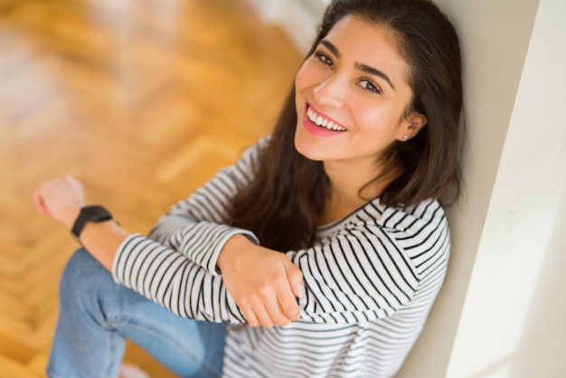 Bella donna bruna sorridente allegra con un grande sorriso che sembra positiva e felice con le braccia incrociate seduta sul pavimento