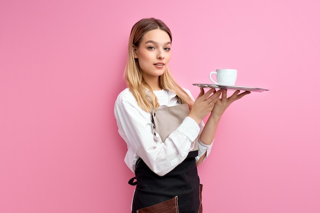 bella donna cameriera in grembiule, che offre una tazza di delizioso caffè gustoso, stare in piedi guardando la telecamera, personale cordiale del ristorante bar.