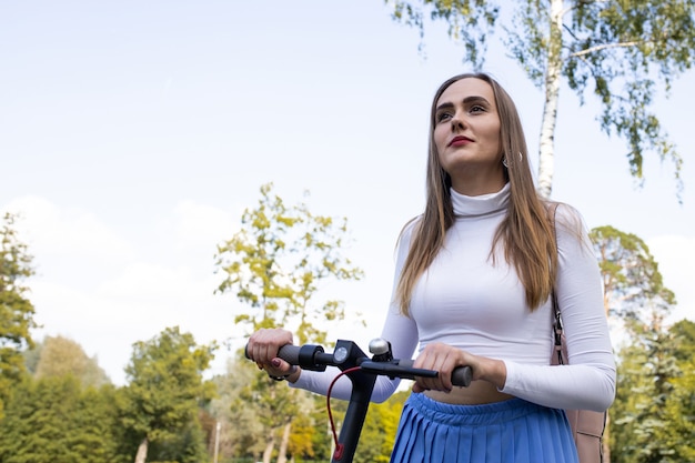 Bella donna cammina lungo il sentiero nel parco e rotola il suo scooter elettrico