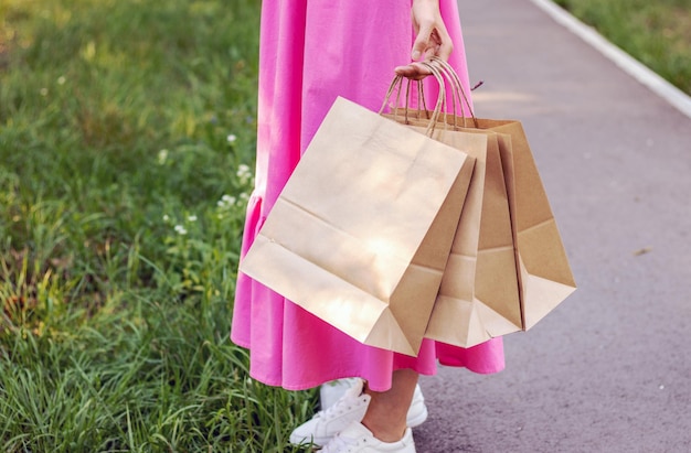 bella donna capelli biondi che cammina nel parco con borse della spesa marrone carta. ragazza in abito rosa sole