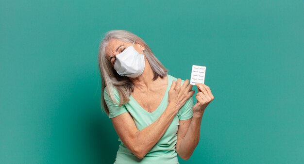 Bella donna capelli grigi con una maschera protettiva e pillole