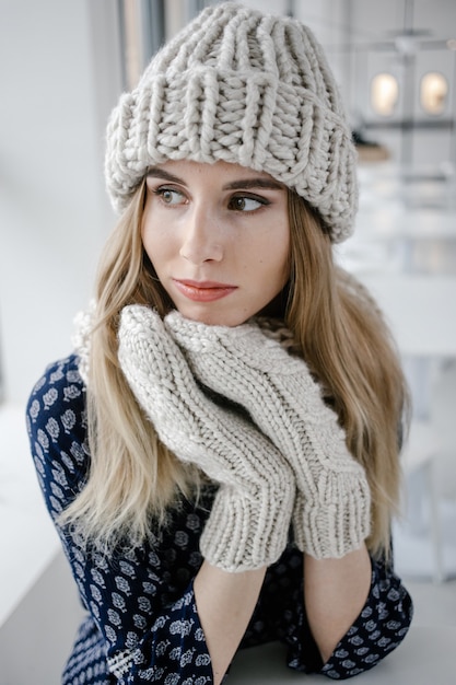 Bella donna carina che indossa cappello invernale lavorato a maglia e guanti su sfondo caffè.