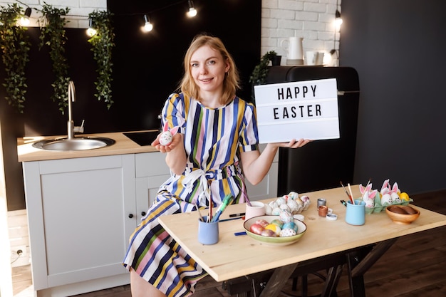 Bella donna casalinga che augura buona Pasqua usando un tablet e tenendo in mano un uovo di Pasqua dipinto La ragazza sta dipingendo e decorando le uova nella sua cucina per le vacanze di Pasqua