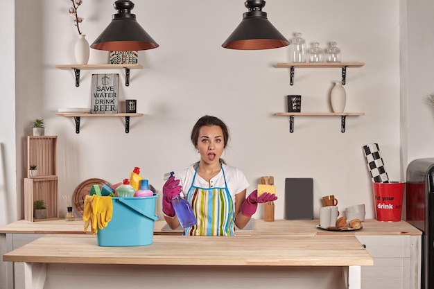 Bella donna castana allegra in guanti che pulisce la cucina moderna