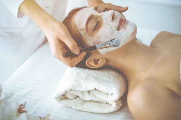 Bella donna castana che si diverte ad applicare la maschera cosmetica con gli occhi chiusi. Trattamento rilassante in concetti di medicina e spa.