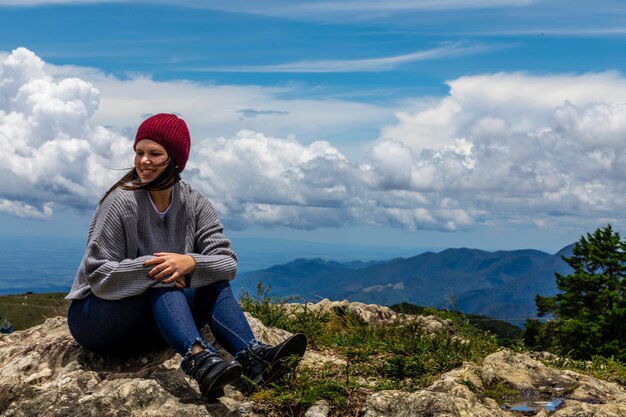 Bella donna castana che si siede sopra la montagna in autunno nelle belle nuvole di superficie