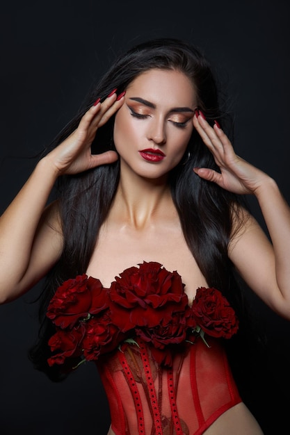 Bella donna castana con un mazzo di fiori di rosa rossa in corsetto rosso. Capelli lunghi, ritratto di body art nudo e sottile