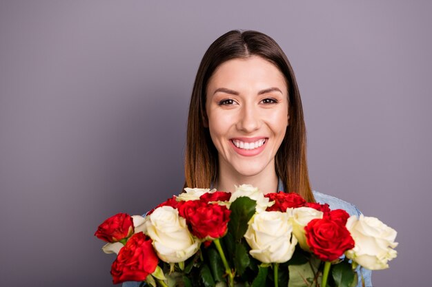 bella donna castana in camicia di jeans in posa con bouquet contro il muro viola