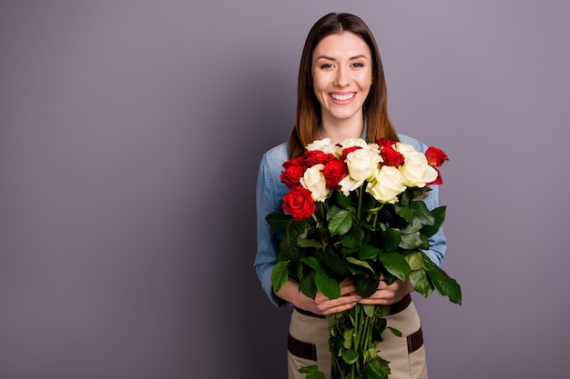 bella donna castana in camicia di jeans in posa con bouquet contro il muro viola