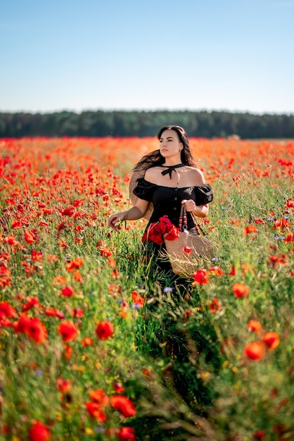 Bella donna castana in un vestito nero con un mazzo di fiori in un campo di papaveri