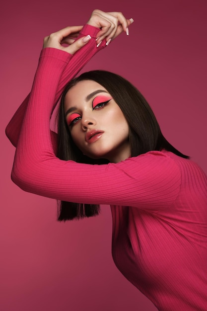 Bella donna castana in vestiti rosa con trucco di moda rosa che posa nel fronte di bellezza dello studio