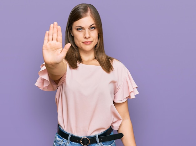 Bella donna caucasica che indossa abiti casual facendo smettere di cantare con il palmo della mano. espressione di avvertimento con gesto negativo e serio sul viso.