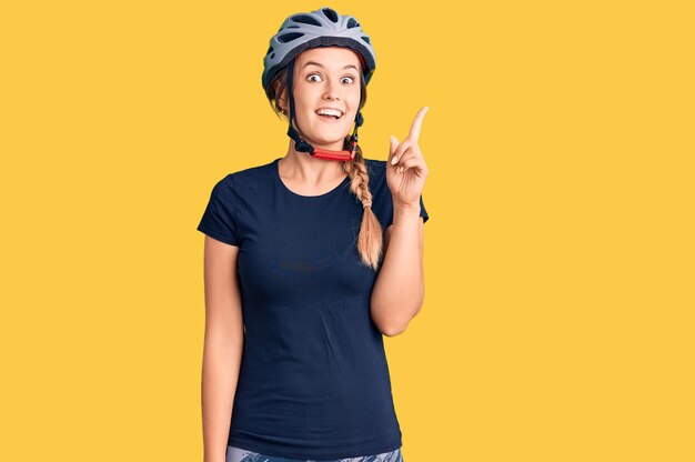 Bella donna caucasica che indossa un casco da bicicletta che mostra e indica con il dito numero uno mentre sorride sicura e felice