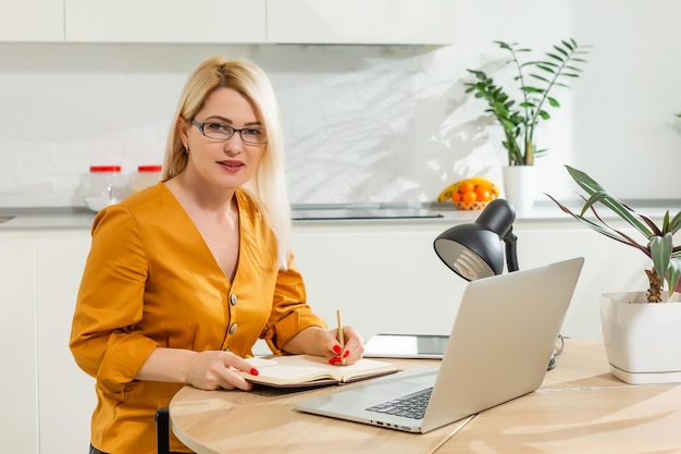 Bella donna caucasica che lavora al computer portatile. Sfondo della cucina.