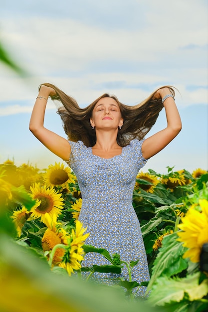 Bella donna caucasica che solleva lunghi capelli scuri nel campo di girasoli