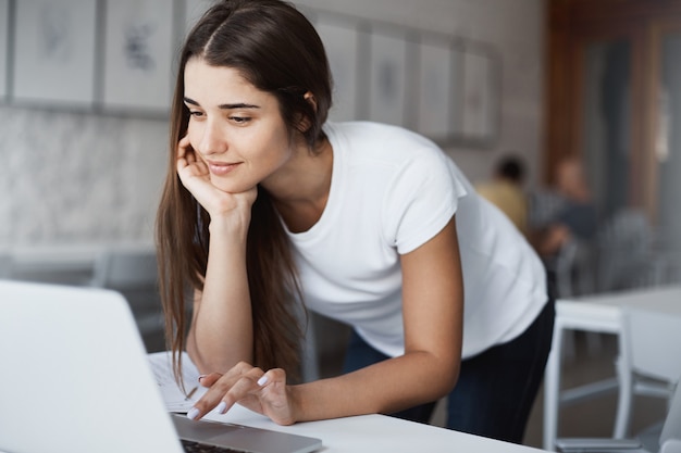 Bella donna caucasica utilizzando il computer portatile sorridente alla ricerca di informazioni su Internet nella biblioteca pubblica.