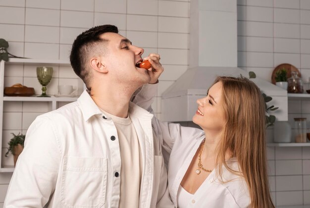 Bella donna che alimenta il marito o il fidanzato mentre cucina insieme nella moderna cucina scandinava r