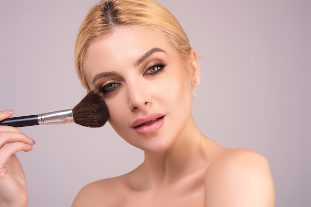 Bella donna che applica la polvere di trucco sulla pelle perfetta della spazzola della polvere cosmetica della guancia e m