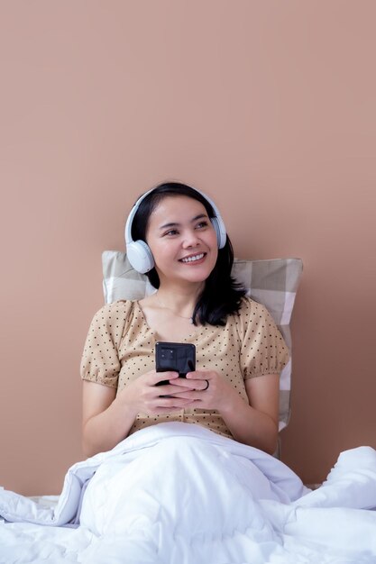 Bella donna che ascolta musica usando le cuffie wireless sul letto mentre guarda la finestra