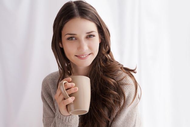 Bella donna che beve caffè al mattino seduta vicino alla finestra