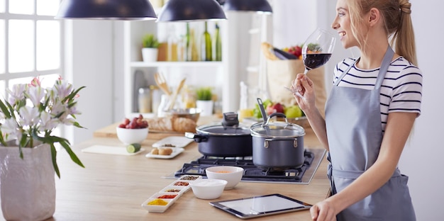 Bella donna che beve del vino a casa in cucina