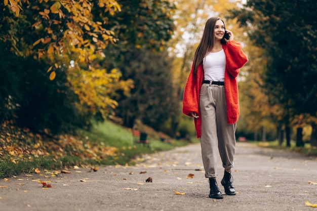 Bella donna che cammina nel parco autunnale e utilizza il telefono