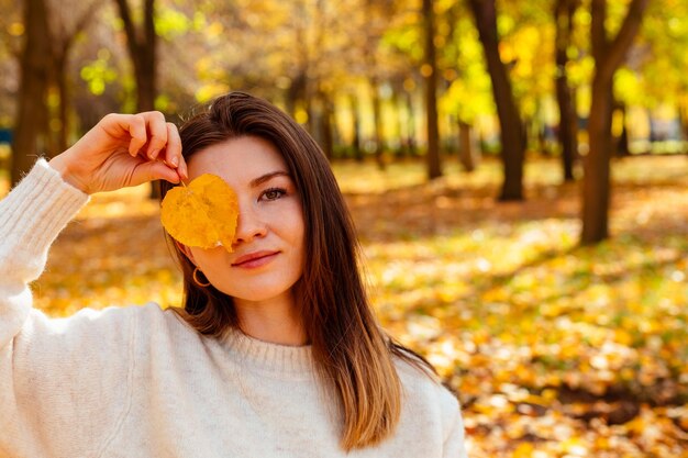 Bella donna che chiude metà faccia con foglia nel parco autunnale