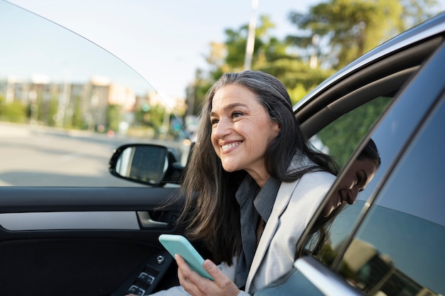 Bella donna che esce dall'auto con uno smartphone con un sorriso felice