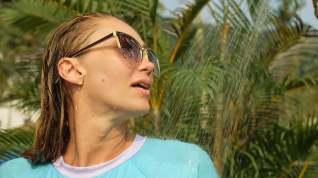 Bella donna che fa la doccia nel giardino vicino all'hotel Ragazza sexy calda in costume da bagno blu lavato via l'acqua salata dai suoi capelli e corpo erotico accarezzandole il seno con le mani Vista ravvicinata