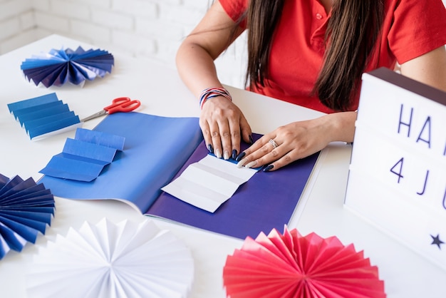 Bella donna che fa rosette di carta fai da te di colori rosso e blu per celebrare il 4 luglio