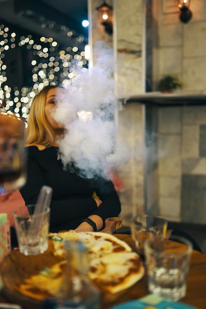 Bella donna che fuma narghilè in un pub donna in abito nero si sta godendo una grande serata al caf...