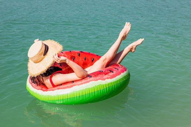 Bella donna che galleggia sull'anello gonfiabile nel giorno soleggiato di estate dell'acqua blu del lago