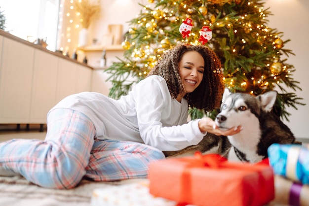 Bella donna che gioca e si diverte con il suo cane mentre si siede vicino all'albero di natale