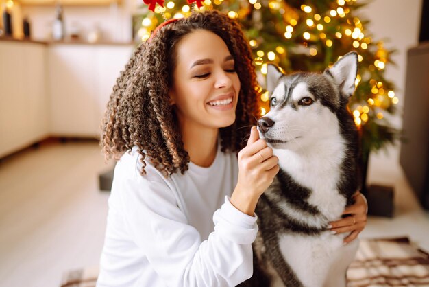 Bella donna che gioca e si diverte con il suo cane mentre si siede vicino all'albero di natale